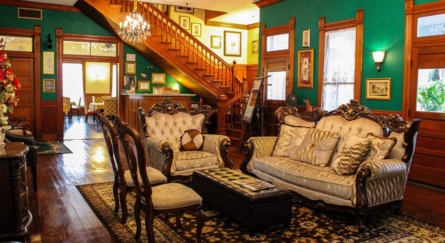 Great room with green walls, wooden wainscotting, hardwood flooring, antique furniture, and large wooden staircase