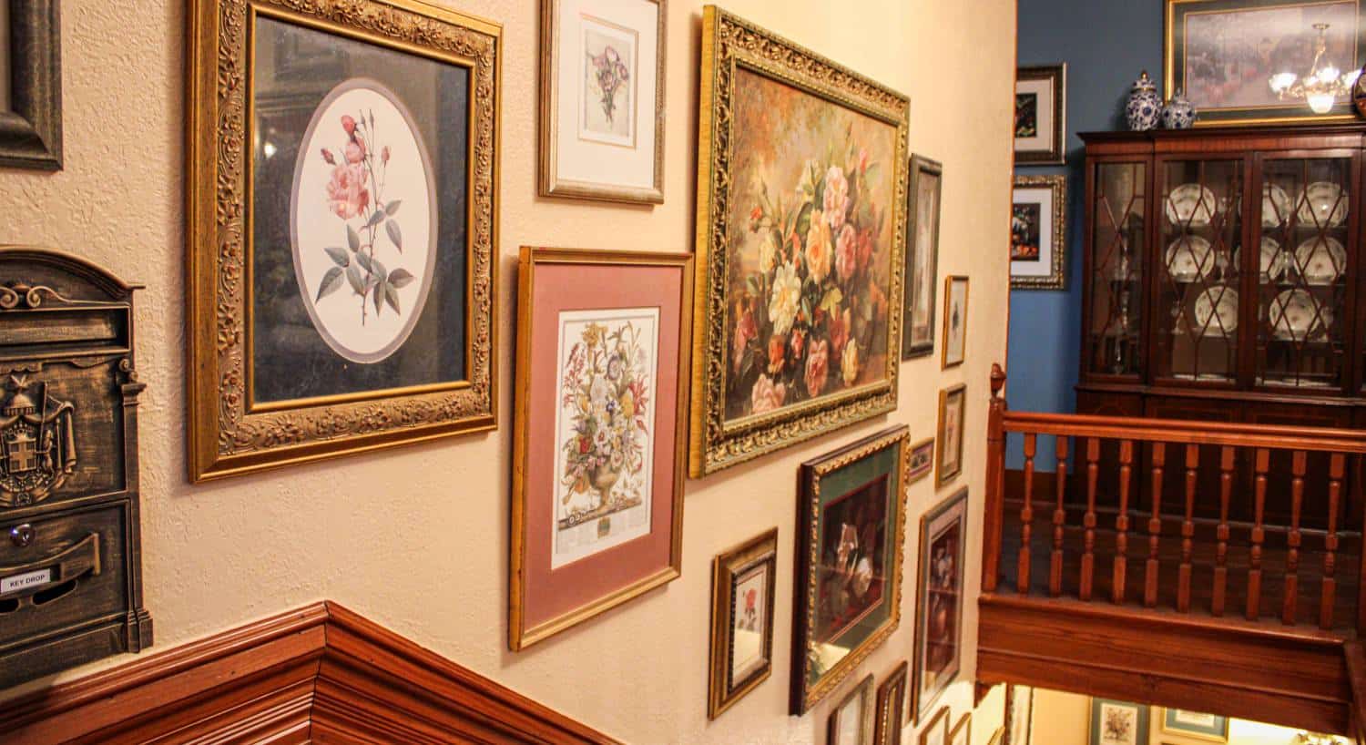 Wall at top of staircase painted cream with multiple framed flower prints and paintings