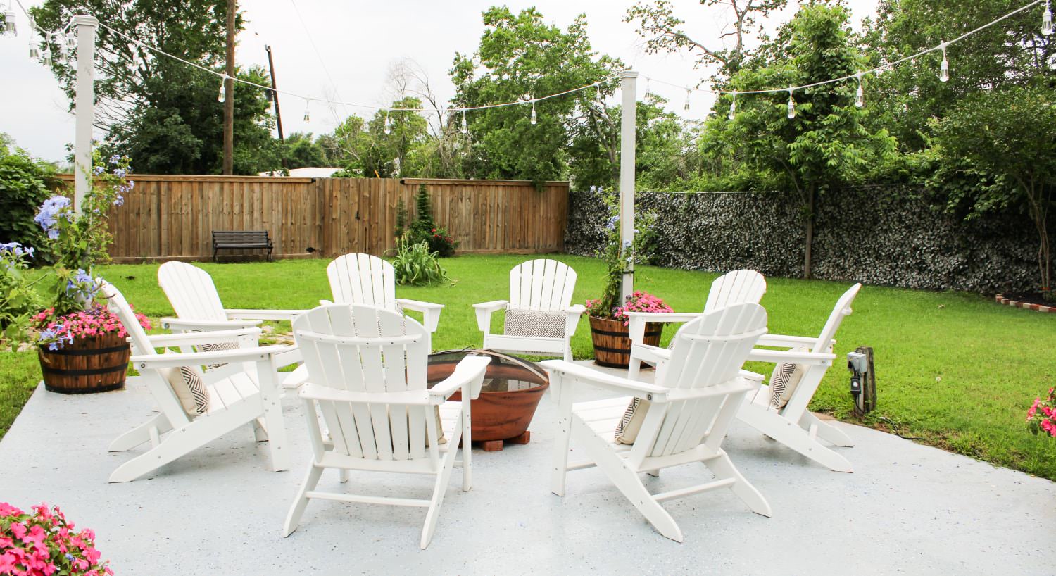 Backyard patio with fire pit, multiple white Adirondack chairs, and green grass