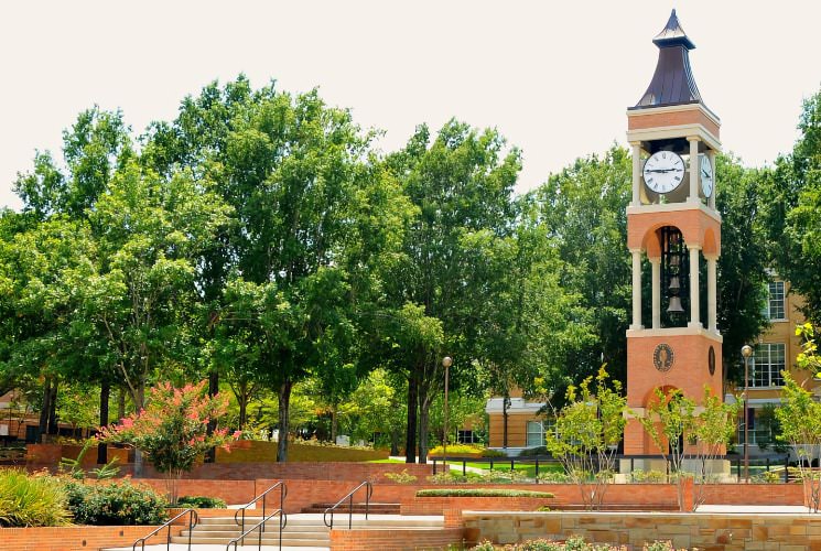 Large light brick clock tower next to large green trees