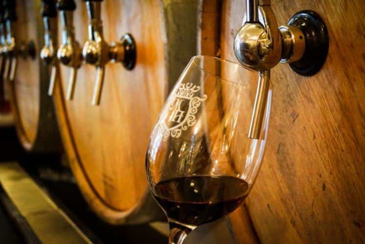 Close up view of a wine glass being filled with red wine from a barrel