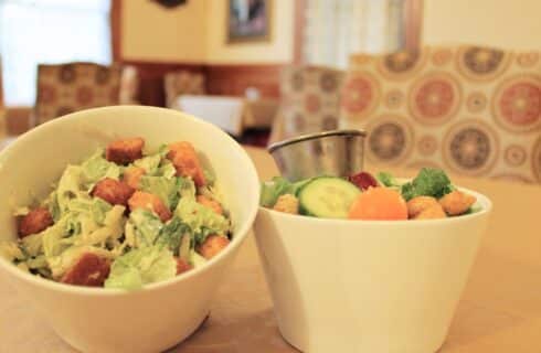 Close up view of two small white bowls, one with a Caesar salad and one with a garden salad