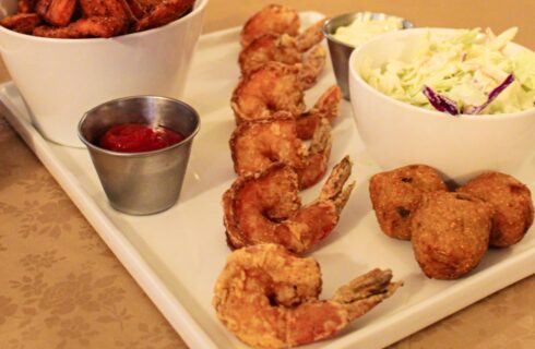 Close up view of battered shrimp, white bowl of coleslaw, and silver cup with cocktail sauce all on a white tray