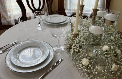 Close up view of a small table with white tablecloth, white flowers, and two placesettings