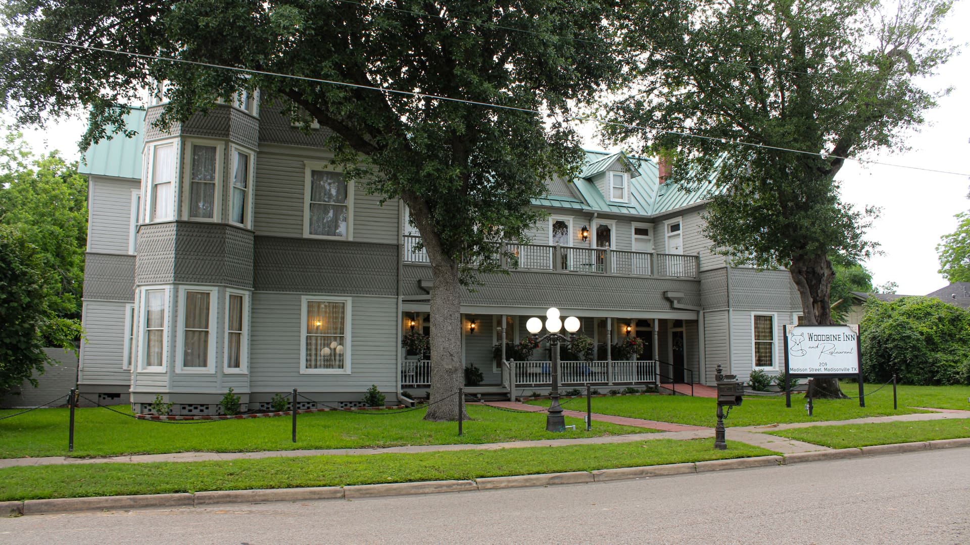 Exterior view of property painted light gray with white and dark gray trim surrounded by green grass and large trees