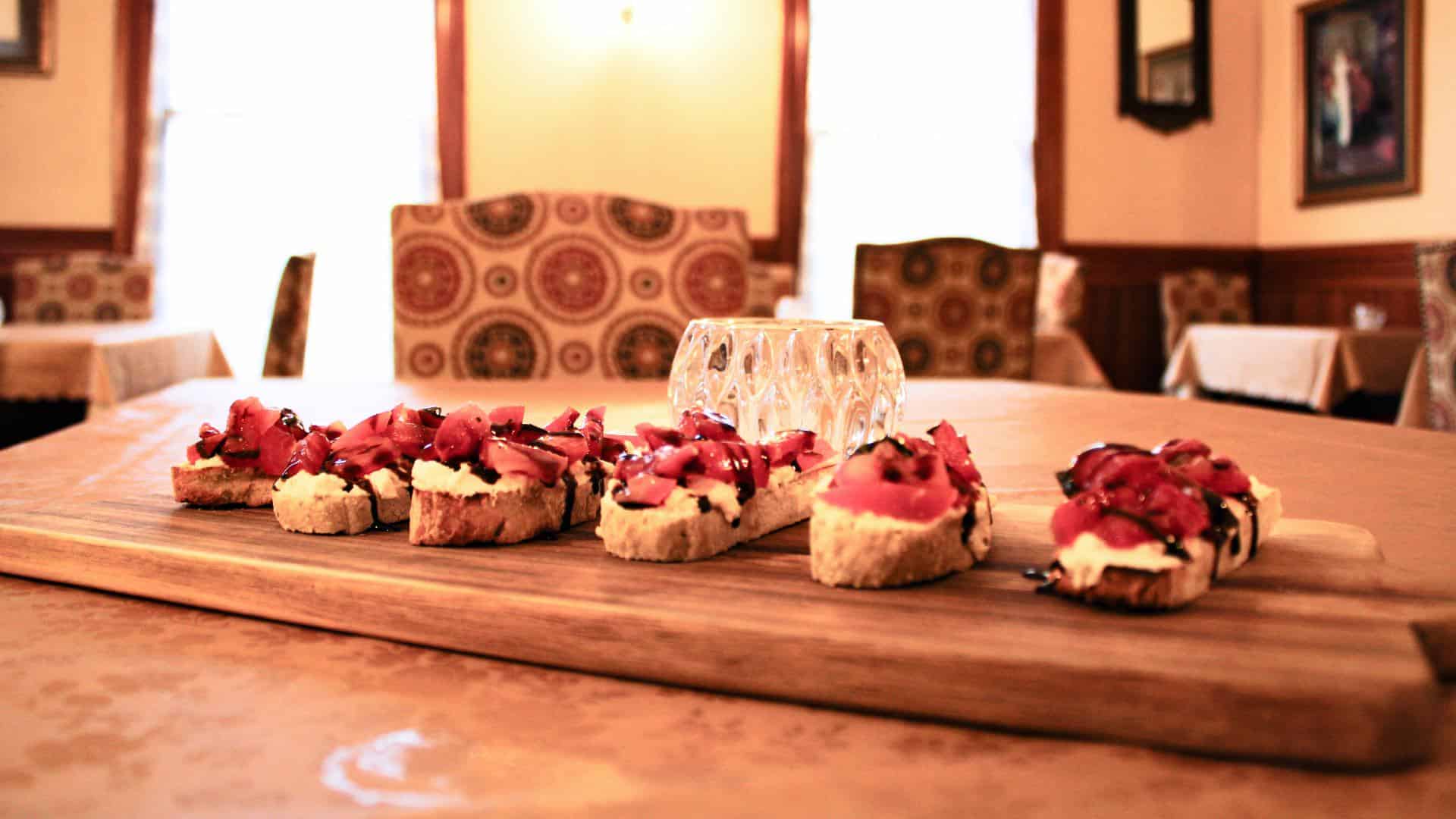 Close up view of toasted bread with cream cheese, strawberries, and chocolate drizzle on wooden board