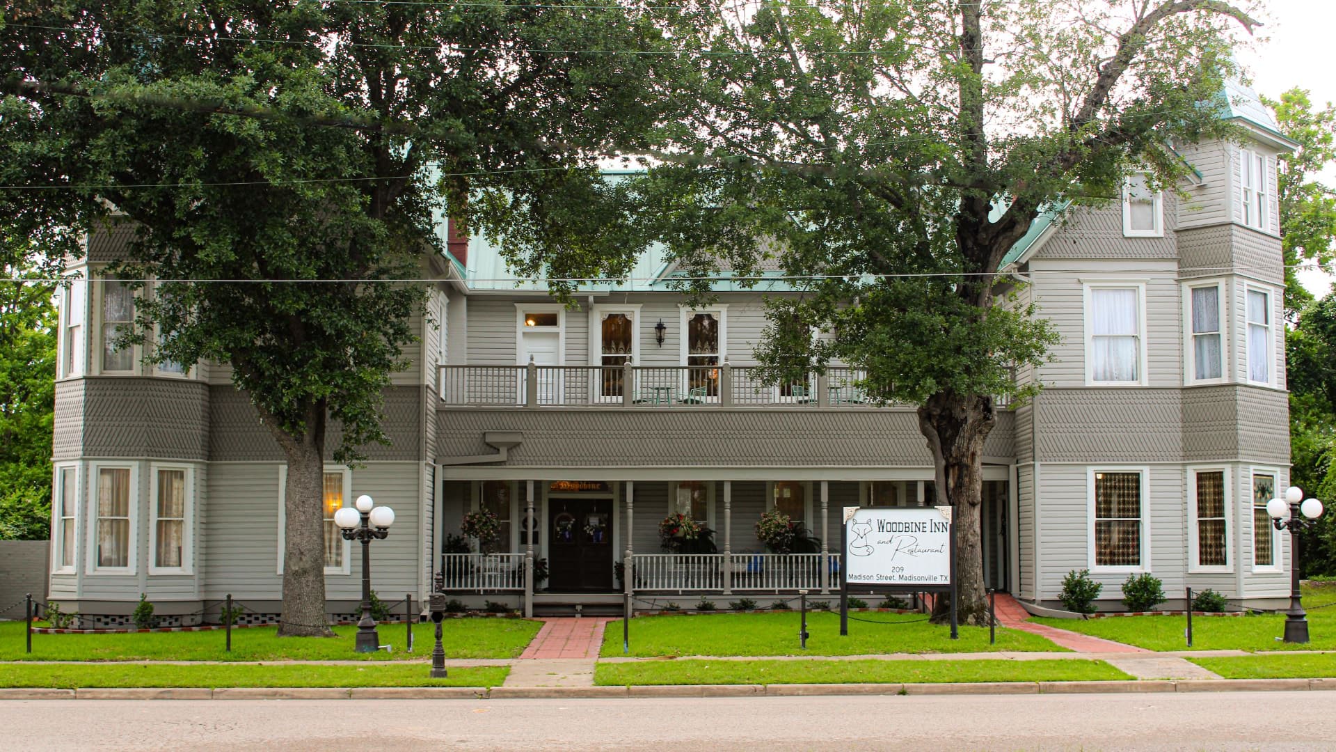 Exterior view of property painted light gray with white and dark gray trim surrounded by green grass and large trees