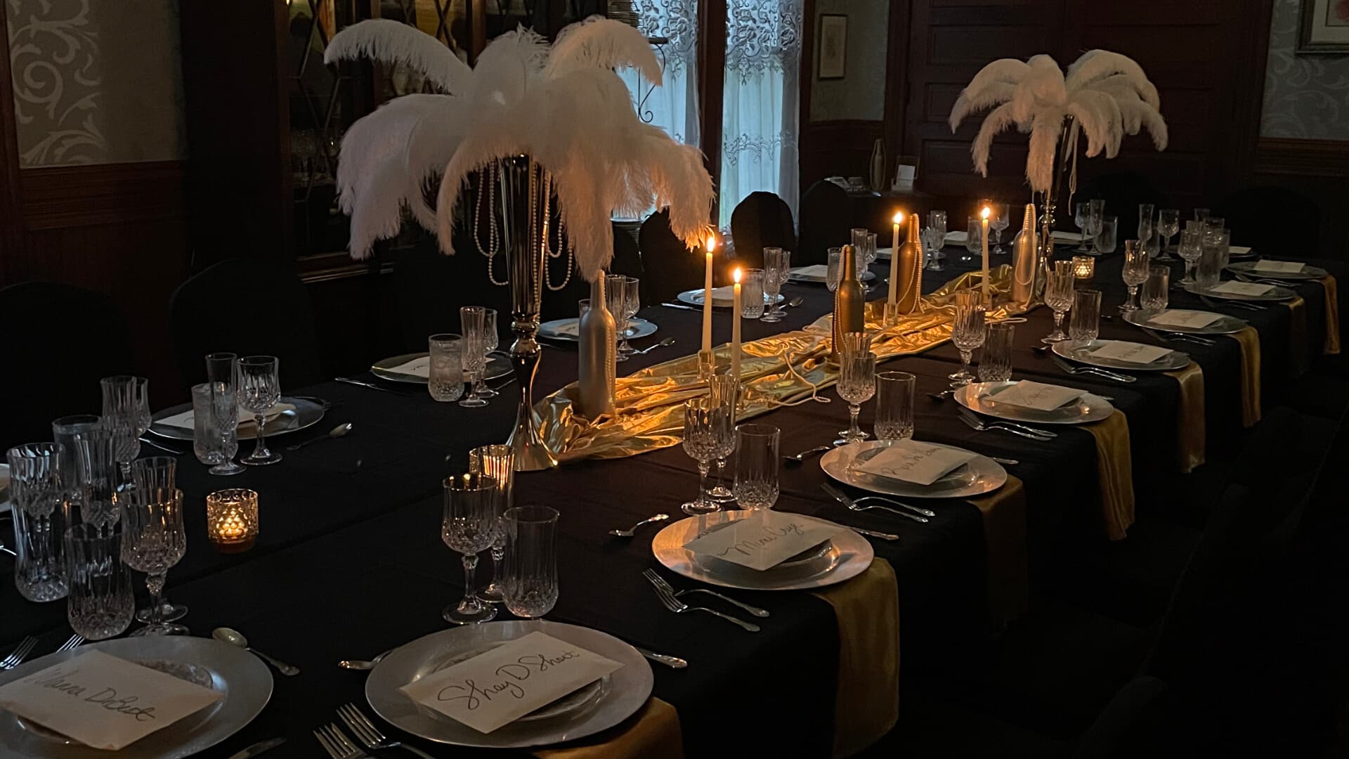 A candlelit table set up for an elegant evening dinner with envelopes with names on the plates, and feather centerpieces.