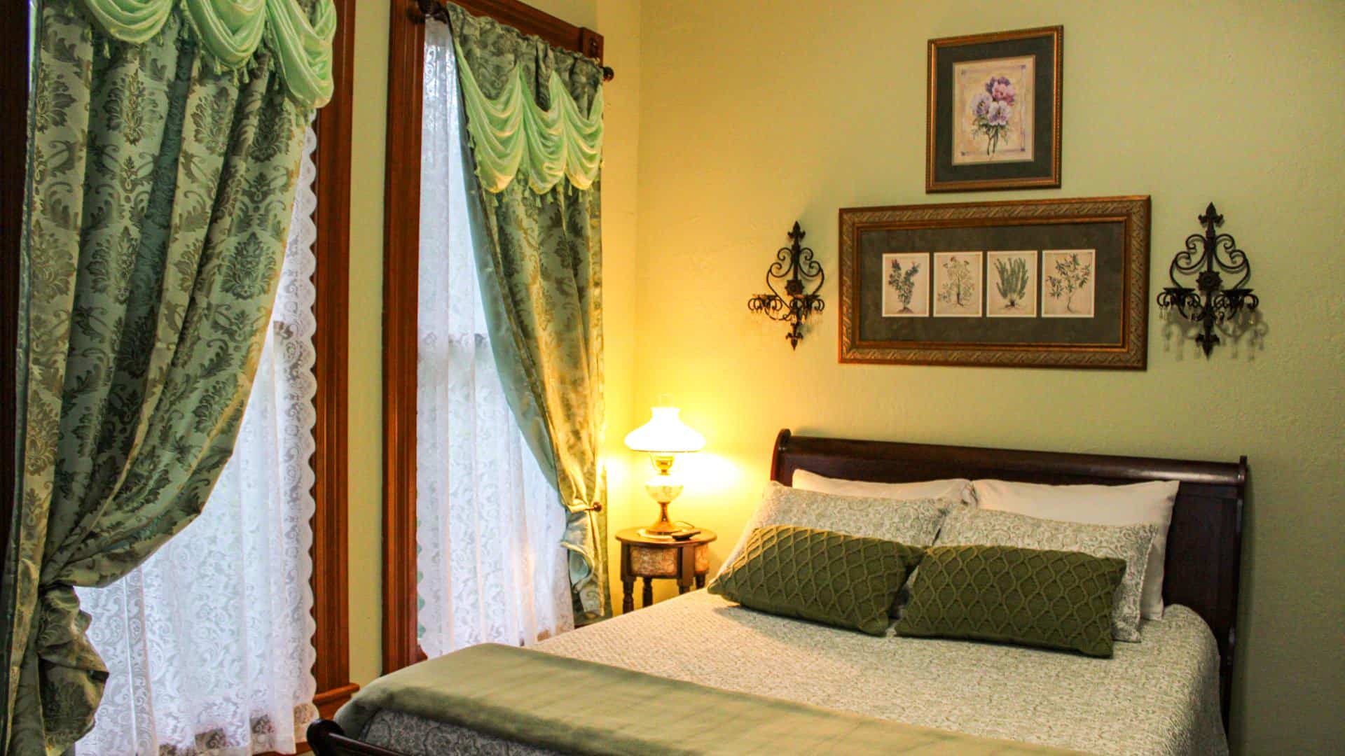 Bedroom with light green walls, dark wooden antique bed, light green bedding, and antique dark wooden nightstand with lamp