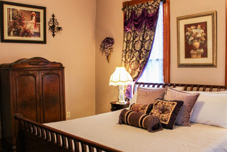 Bedroom with light-colored walls, hardwood flooring, dark wooden sleigh bed, white bedding, and antique dark wooden hutch