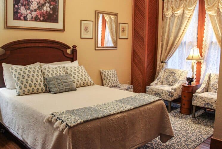 Bedroom with cream walls, hardwood flooring, dark wooden antique bed, white bedding, and sitting area