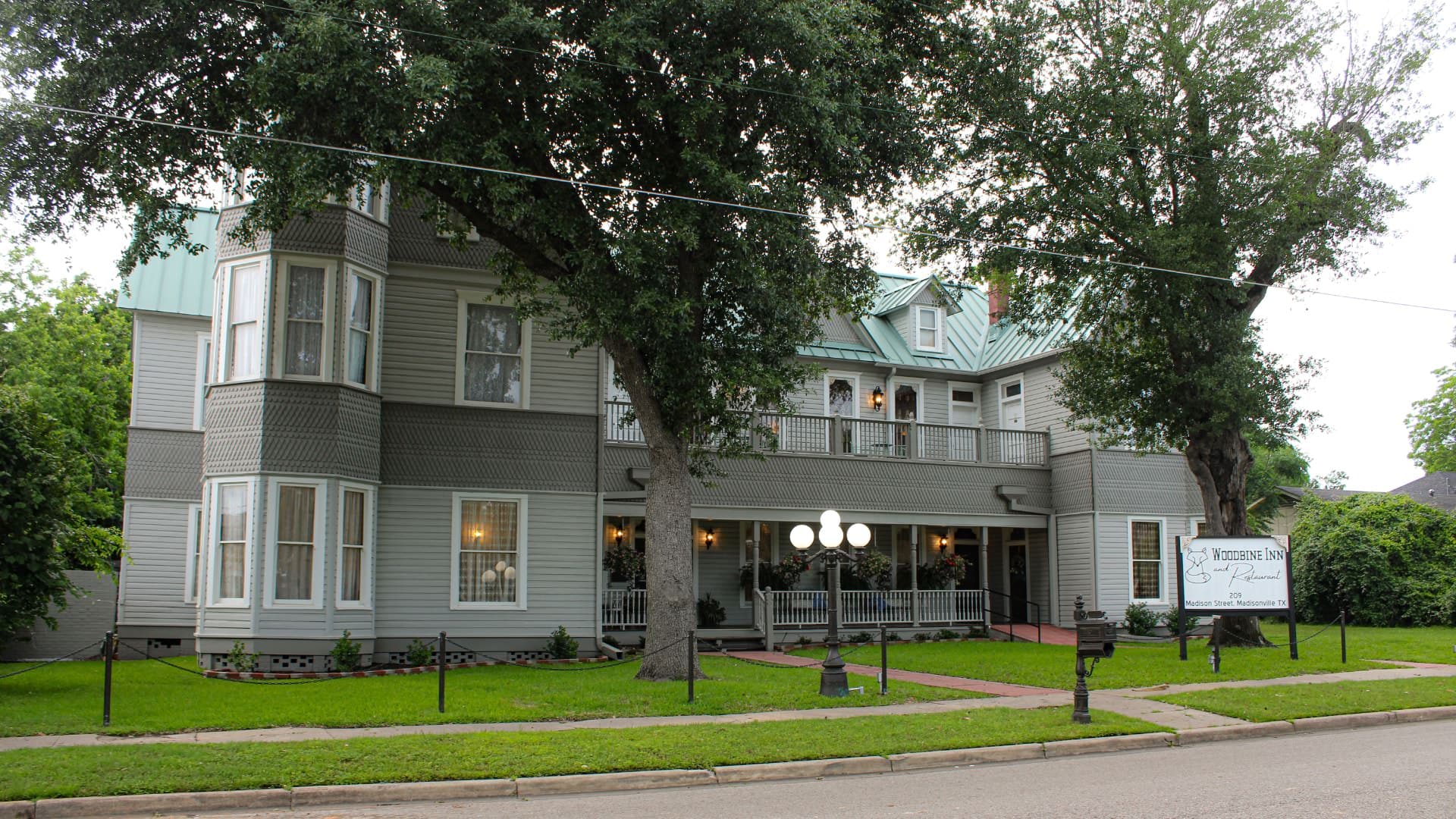 Exterior view of property painted light gray with white and dark gray trim surrounded by green grass and large trees