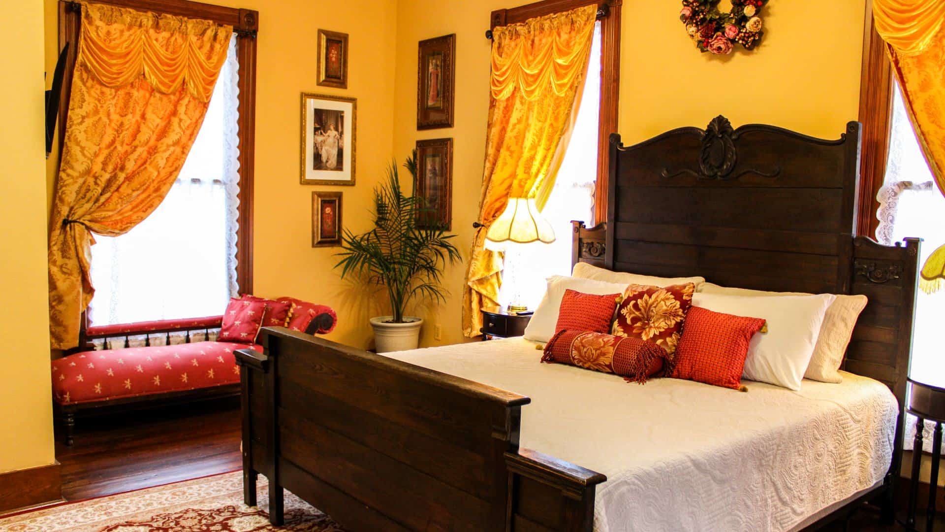 Bedroom with yellow walls, hardwood flooring, dark wooden antique bed, white bedding, and antique chaise lounge