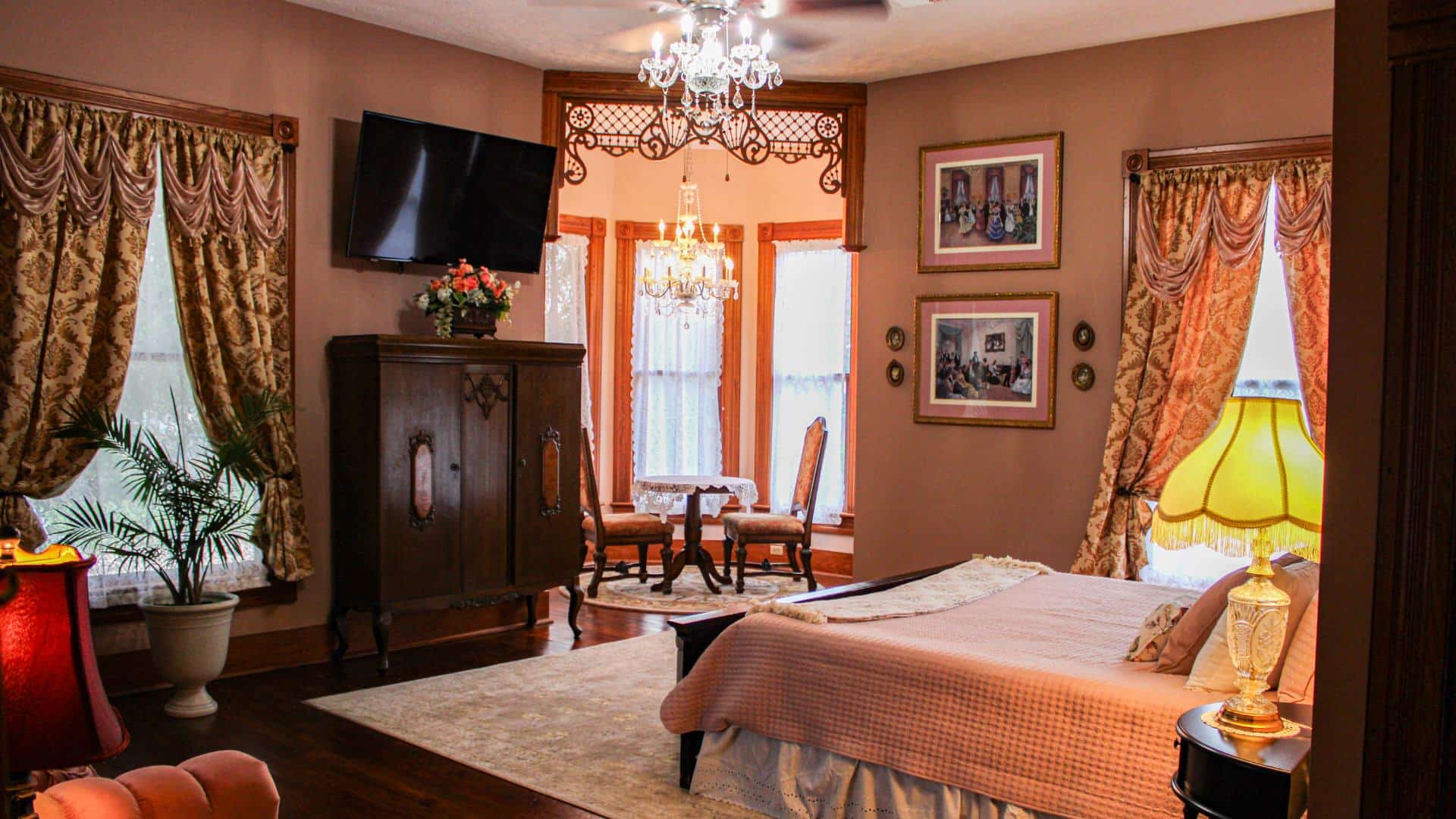 Bedroom with light pink walls, hardwood flooring, dark wooden bed, pink comforter, vintage wooden cabinet, and wall-mounted TV