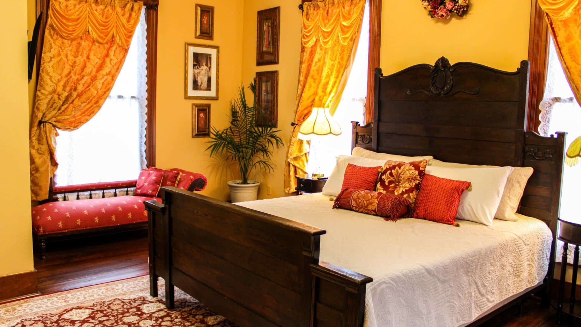 Bedroom with yellow walls, hardwood flooring, dark wooden antique bed, white bedding, and antique chaise lounge