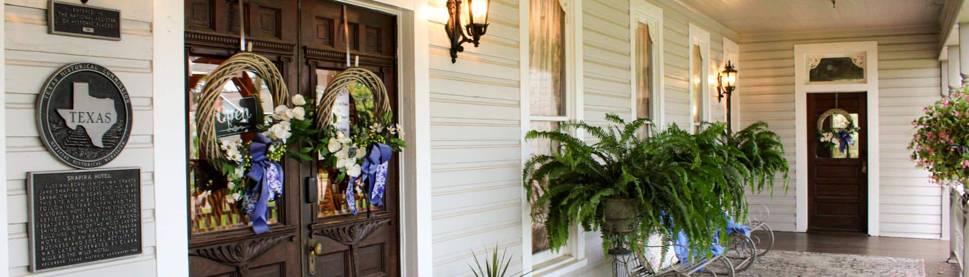 Front porch of property with double wooden main entrance door, metal benches, and potted plants