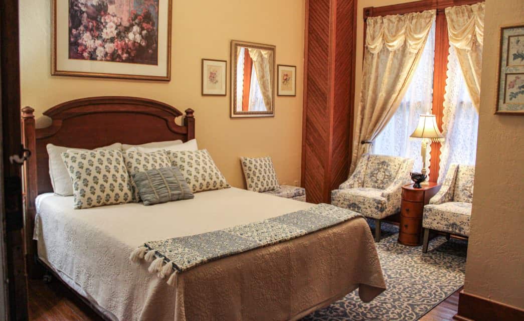 Bedroom with cream walls, hardwood flooring, dark wooden headboard, white bedding, and sitting area