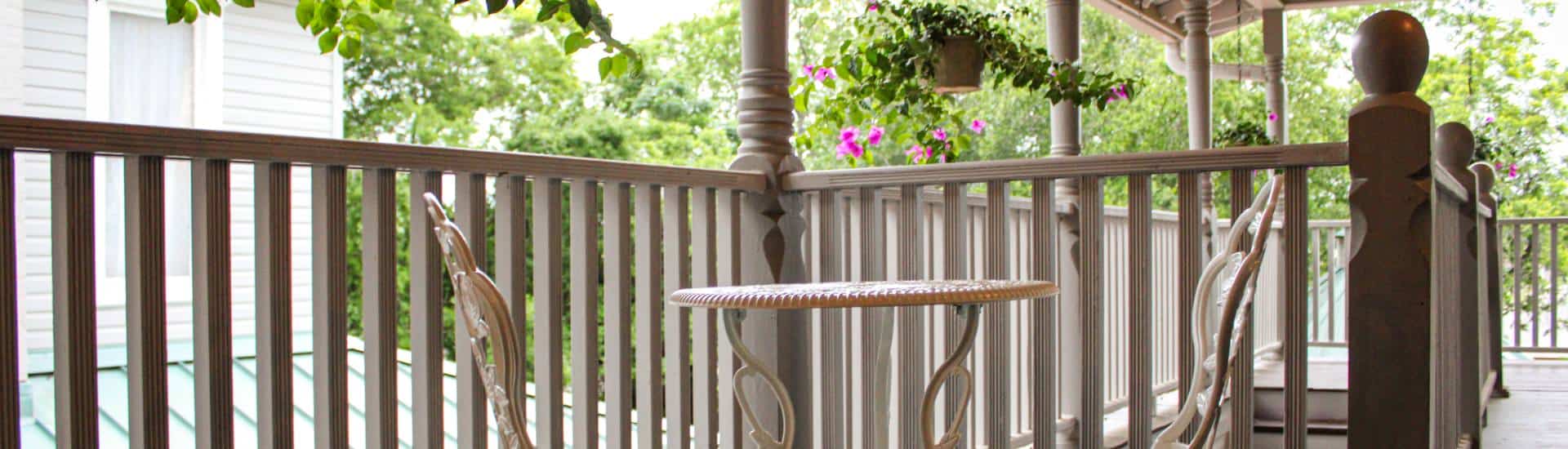 Upper level covered deck with white wrought iron table and chairs and hanging flower baskets